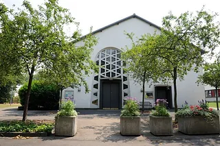 Weiße Kirche mit rundem Fenster und Bäumen.